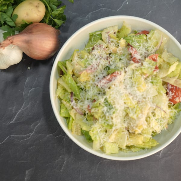 A fresh Italian salad with lettuce, tomatoes, and cheese, next to garlic, potato, and onion.