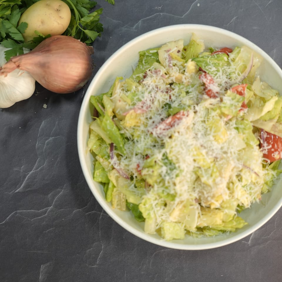 A fresh Italian salad with lettuce, tomatoes, and cheese, next to garlic, potato, and onion.