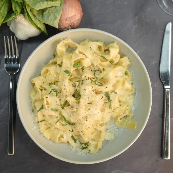 Creamy fettuccine alfredo with grated cheese and fresh herbs, next to a fork and knife.