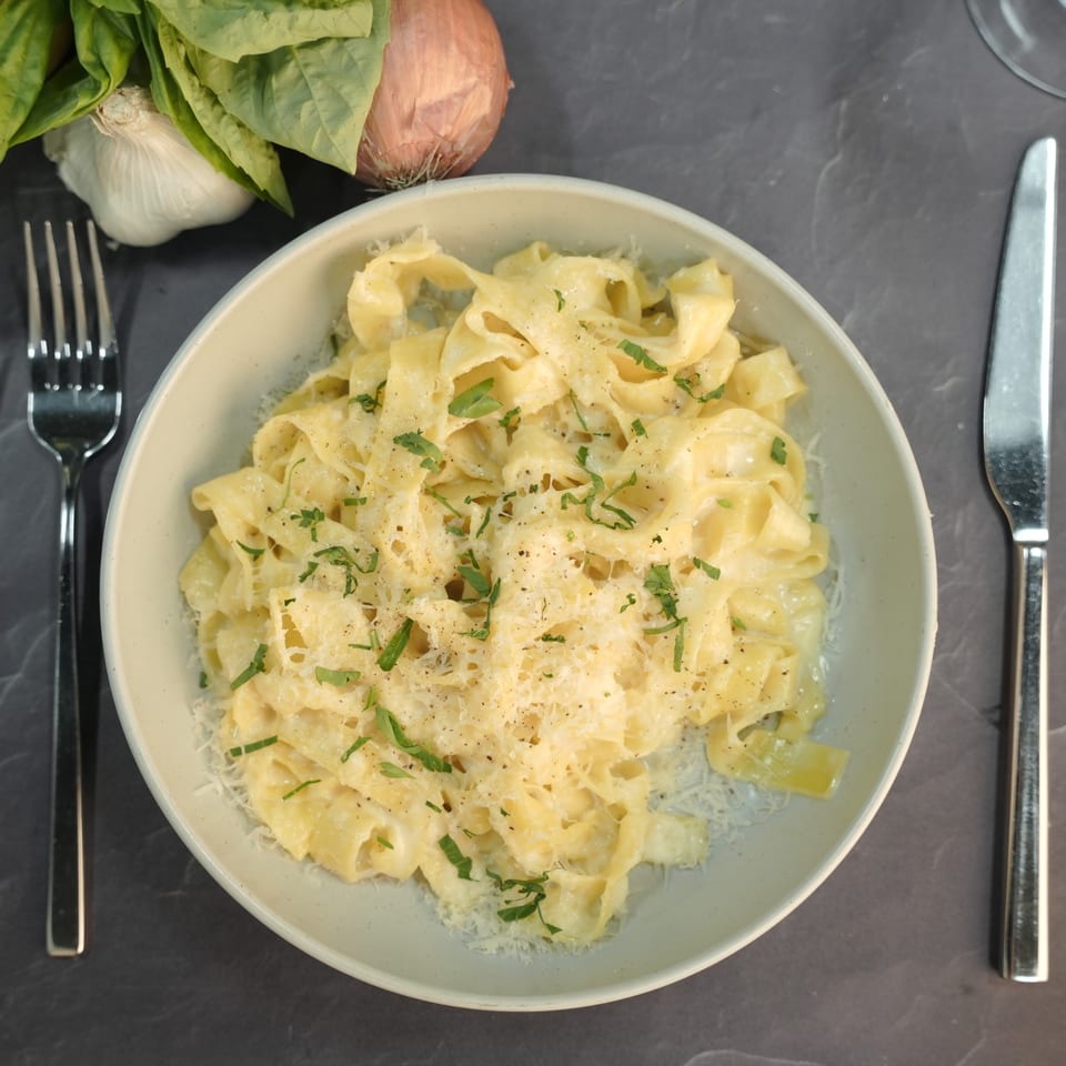 Creamy fettuccine alfredo with grated cheese and fresh herbs, next to a fork and knife.