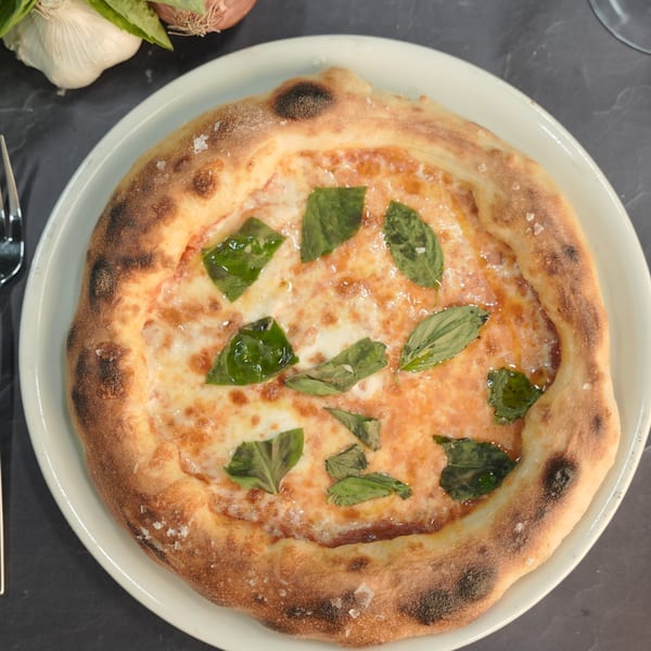 Grano's Italian Margherita pizza with fresh basil leaves and melted cheese on a white plate.